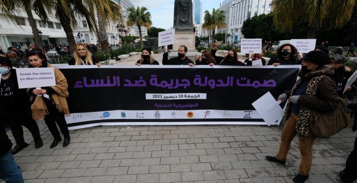 Protestsers stand behind a giant placard reading : The silence of the state is acrime against women.